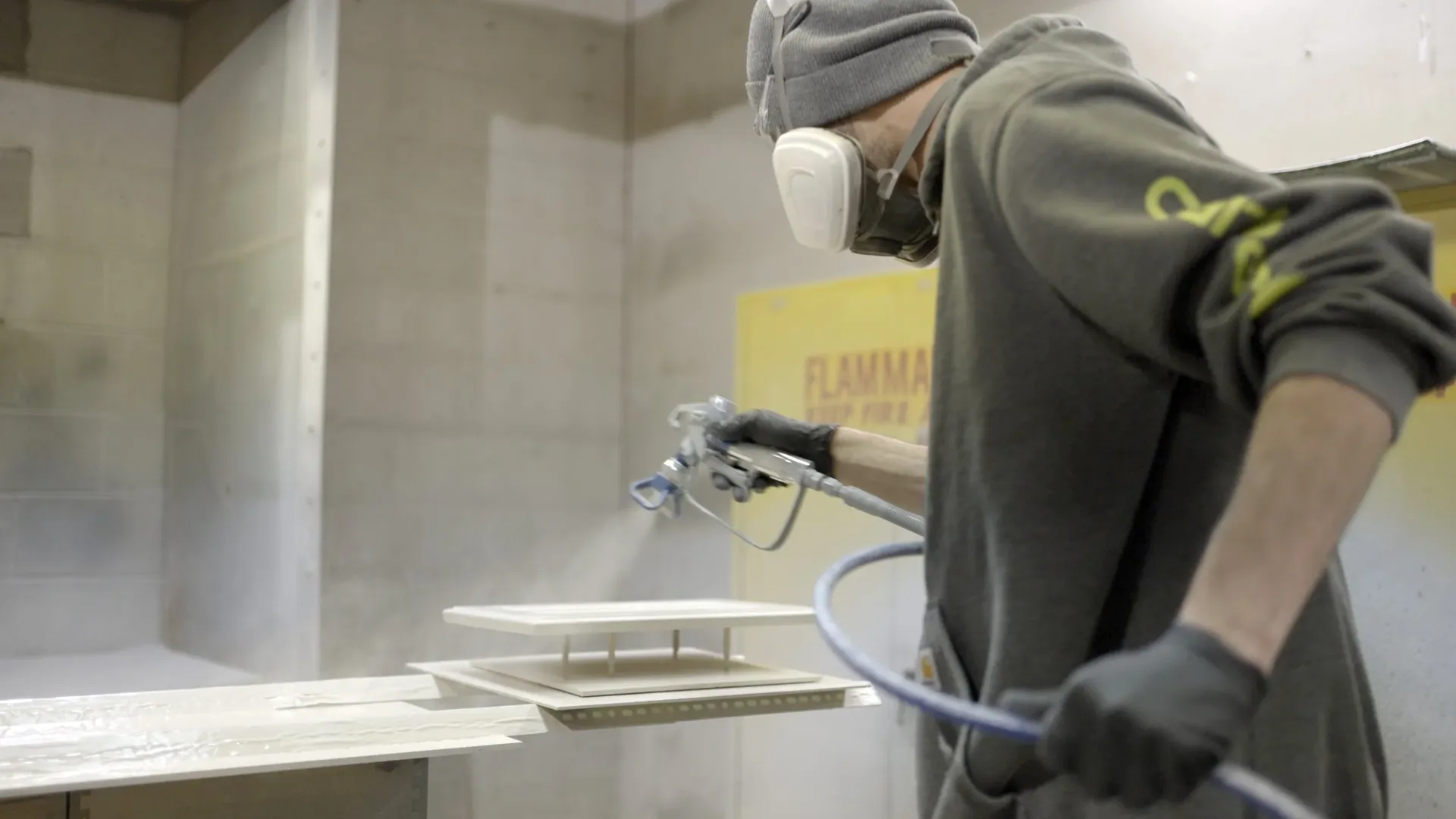 A worker spray paints a section of kitchen cabinets.