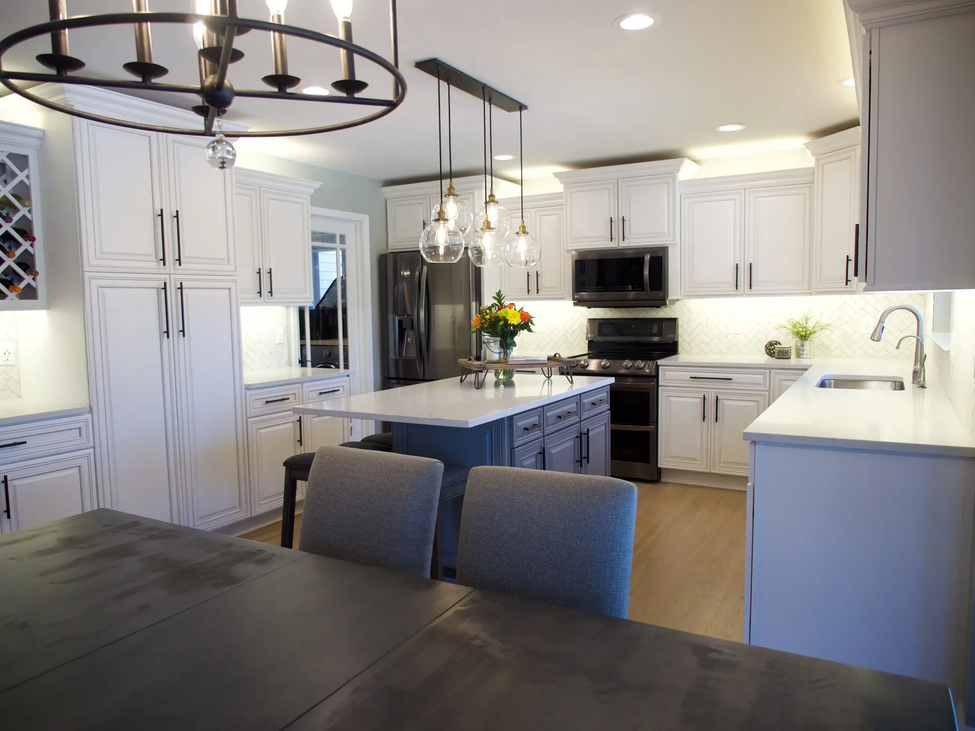 A white kitchen with newly-painted cabinets, black fixtures, central island with bar stool seating, and white countertops.