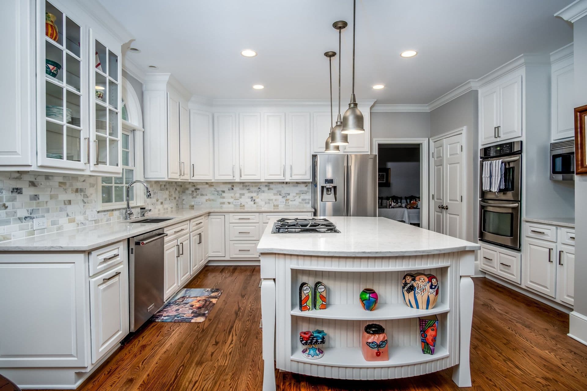 A kitchen with newly-painted white cabinets, light-colored tile backsplash, large central island, and stainless steel appliances.