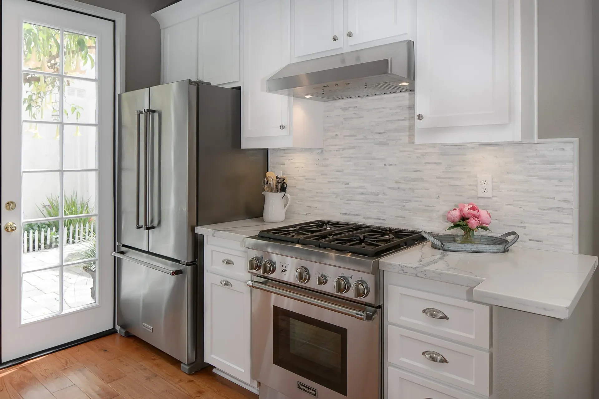 A kitchen with newly-refaced white cabinets, stainless steel appliances, and white tile backsplash.