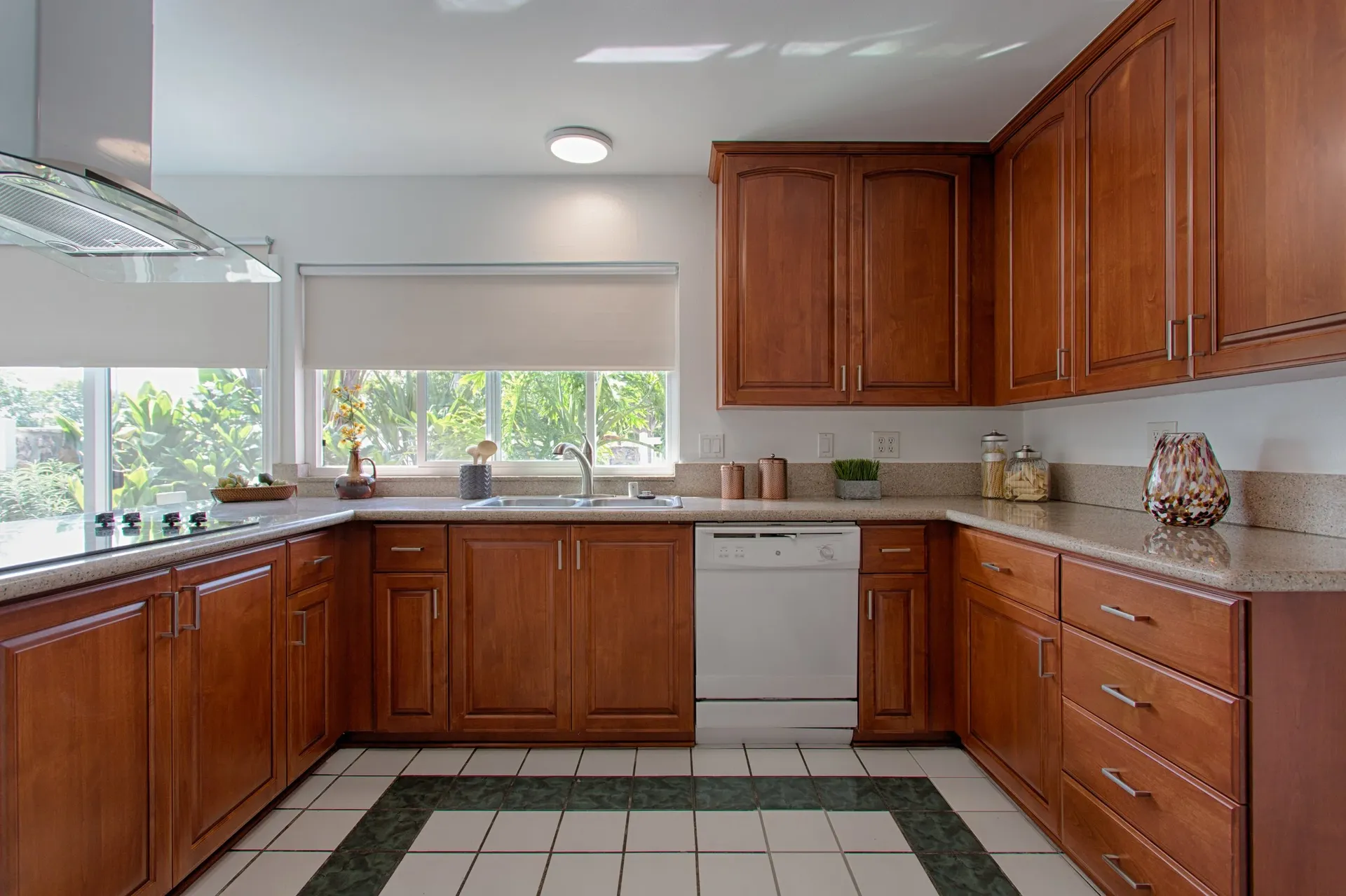 A kitchen with newly-refaced medium brown cabinets, sand-colored countertops, and white and green tile floor.